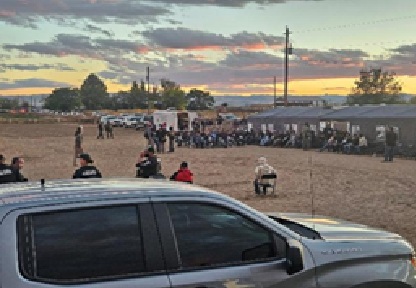 Large group of detained individuals sitting outdoors at dusk surrounded by law enforcement