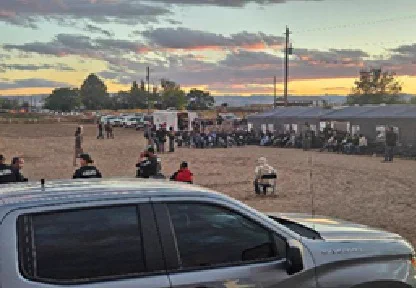 Large group of detained individuals sitting outdoors at dusk surrounded by law enforcement